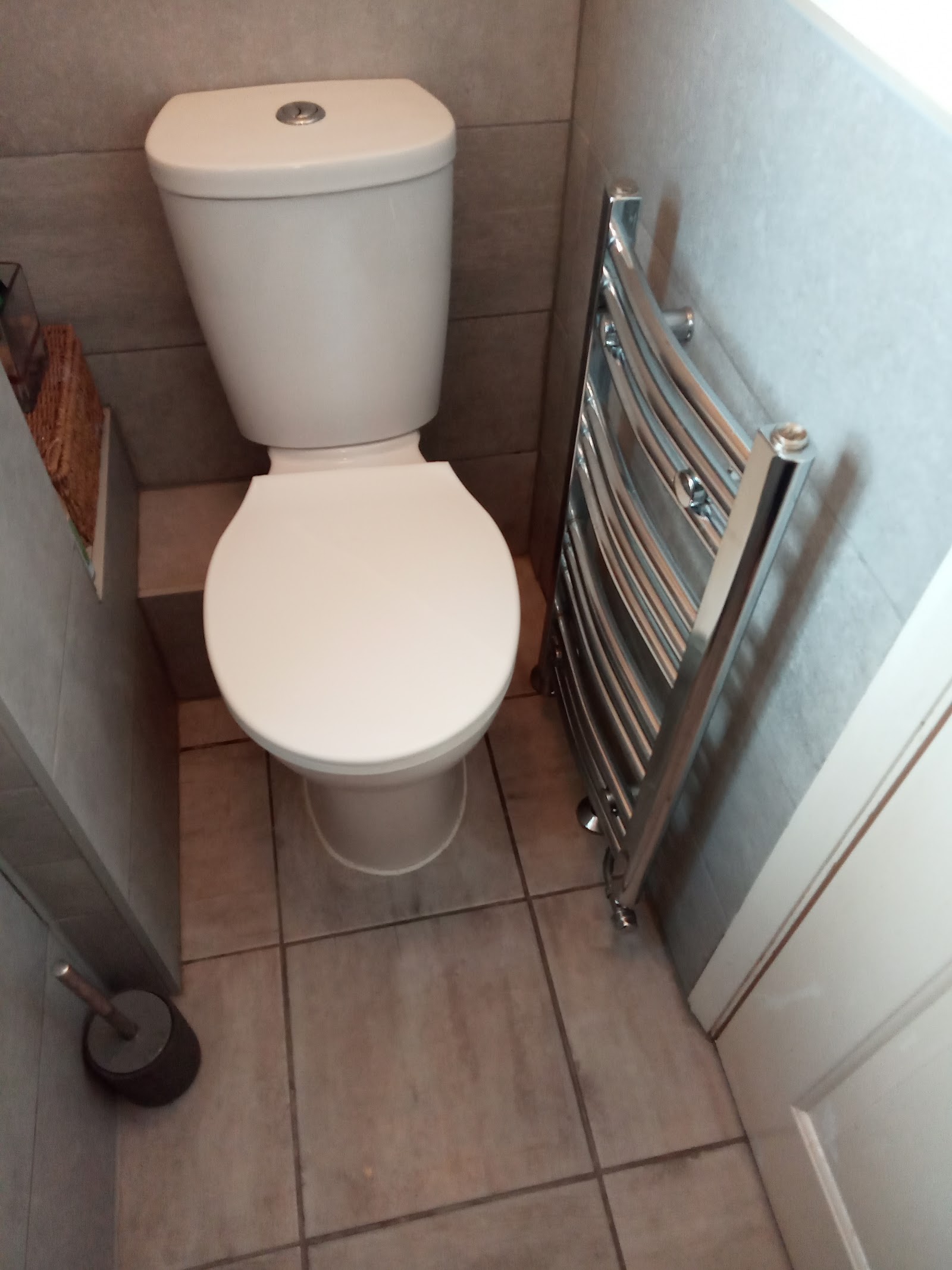 A toilet and new chrome heated towel rail fitted in a tiled bathroom by AbbeyCliffe